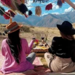 Viajeras disfrutando un picnic andino con vino y quesos frente a las montañas de Maras